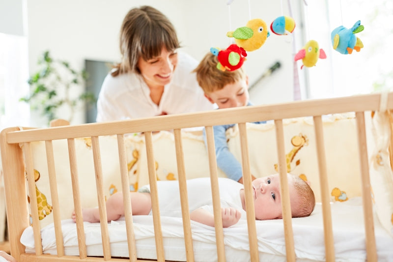 Mutter und Bruder am Babybett schauen auf neugeborenes Baby im Kinderzimmer